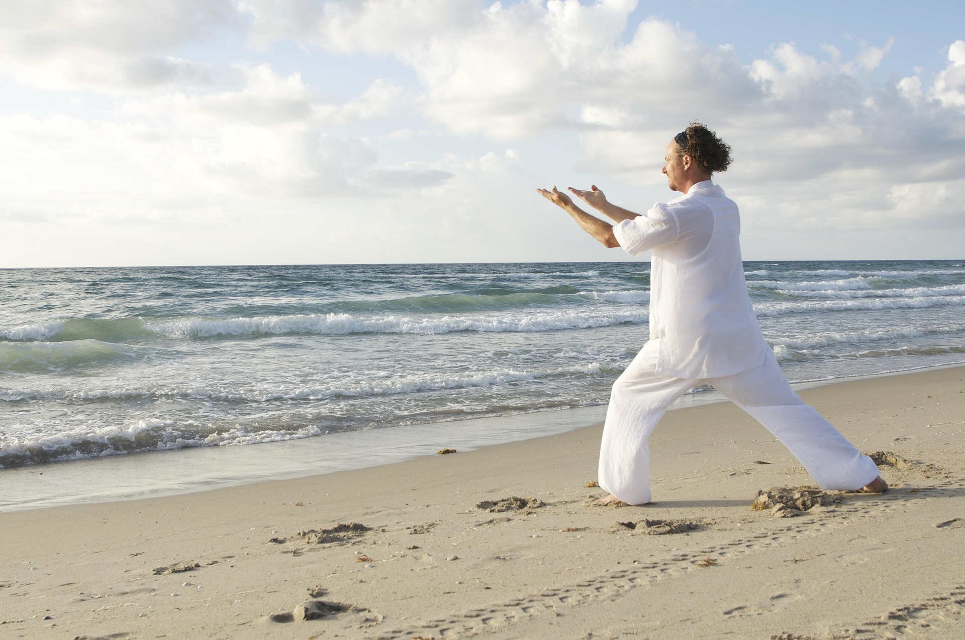 Bilden visar en person på en strand som utövar tai chi eller yoga.